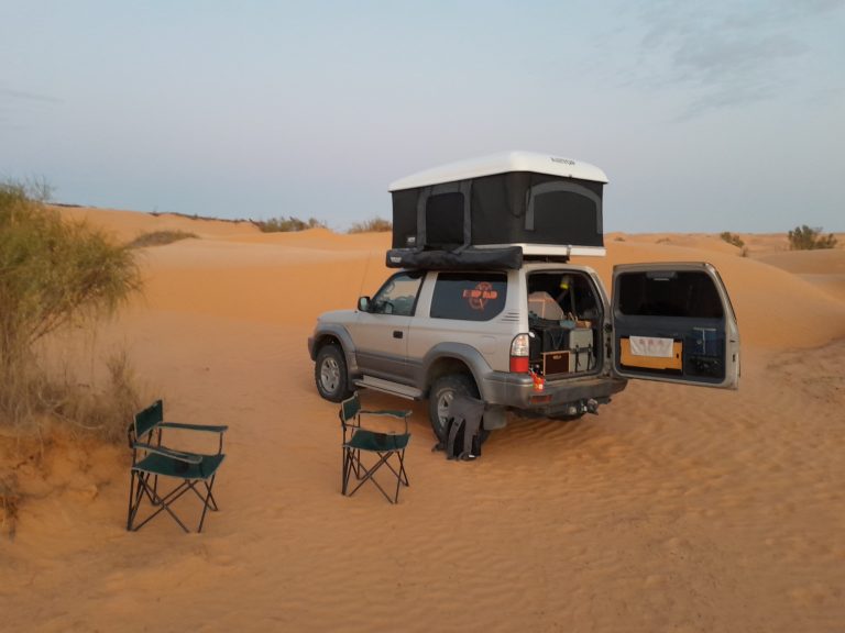 Photo d'un 4x4 avec une tente de toit et le coffre ouvert avec deux chaises pliante à côter