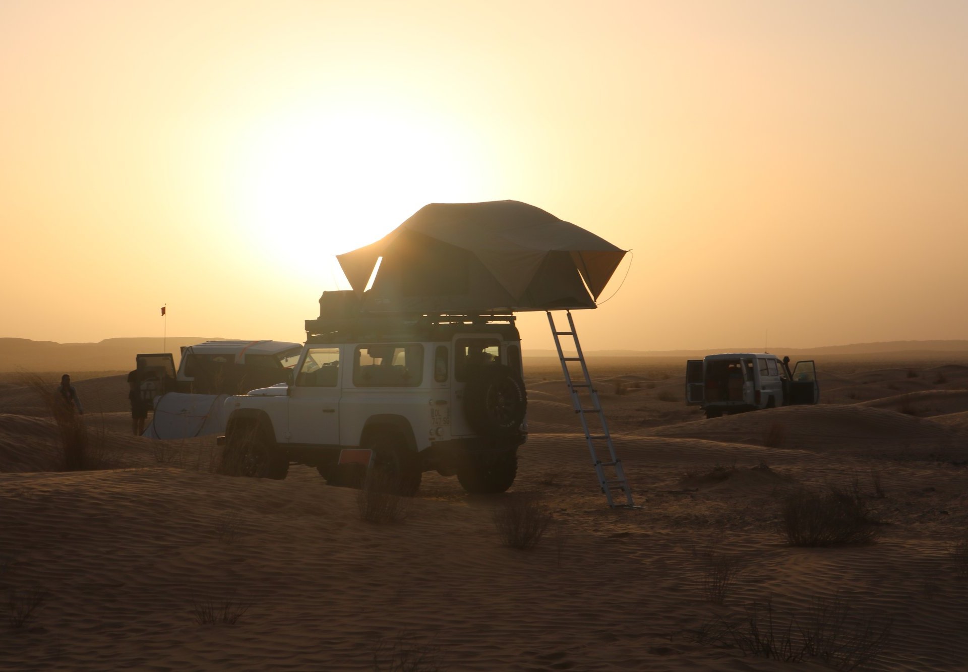 Photo d'un 4x4 pris de dos avec une tente de toit et une échelle dans les dunes de Tunisie